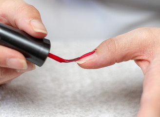 Close up of the nail enamel brush with red lacquer coating a single finger nail