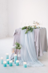 The composition of pine decoration suspended on the ceiling, candles, flowers and greenery standing on served table in the area of wedding party