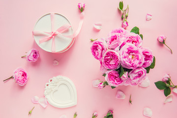 Top view pink tea roses bouquet, white round box with ribbon and vintage photo frame in shape of heart on pink background. Festive Gift. Celebrating love. Postcard mock up. Copy space.