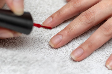 Obraz na płótnie Canvas Girl lacquering her finger nails with red nail enamel on a white towel