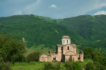 Fototapeta premium the ancient Christian Sentinian temple of the 10th century in the Karachay-Cherkess Republic against the background of green, overgrown mountains.
