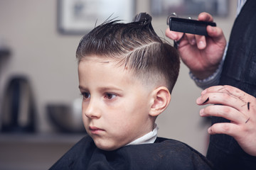 Barber making hairstyle to a Caucasian boy using scissors and hairbrush. - 209934409