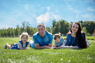 Fototapeta premium Cheerful family in a park, parents and their two children are lying on the grass. Shot with flare
