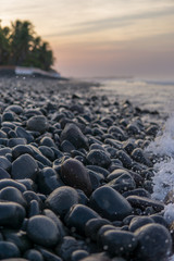 Obraz premium Ocean splash with a lot of foam on dark rocks at sunrise.