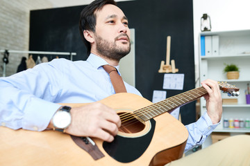 From below shot of trendy man in suit playing guitar in relax sitting at working place and dreaming. 