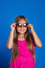 Portrait of young pretty girl in pink dress, sunglasses and hat on blue background . Summer vacation and travel concept