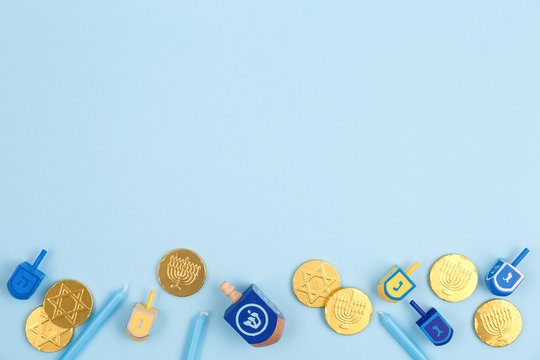 Blue background with multicolor dreidels, menora candles and chocolate coins. Hanukkah and judaic holiday concept.