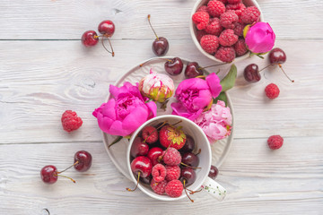 raspberries, cherries and strawberries in bowls, flavors of summer with peony flowers