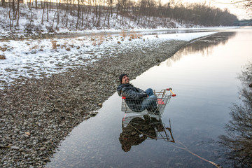 Mann sitzt grinsend in Einkaufswagen, im Fluss geparkt