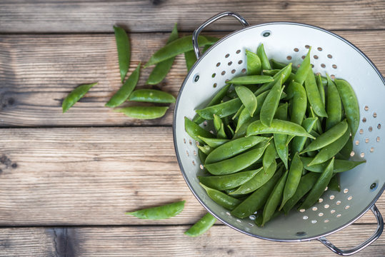 sugar snap peas in a white colander on a wooden table