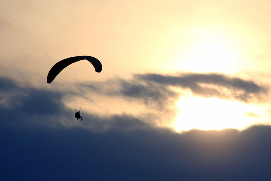 Paraglider flying on a wing in the sky against the setting sun