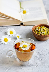 Cup of tea with chamomile flowers on gray background, book reading, free time concept