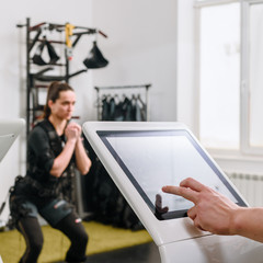 Coach pushing on screen on EMS machine while woman waiting for training, focus is on fingers