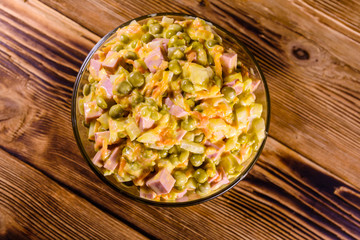 Salad with sausage, green pea, onion and carrot in glass bowl on wooden table. Top view