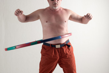 Funny Elderly retired man, aged 60 years old, with Santa Claus hat and sunglasses, is engaged in physical exercises with dumbbells and hoop. Concept of healthy lifestyle. Holiday time. Christmas Eve