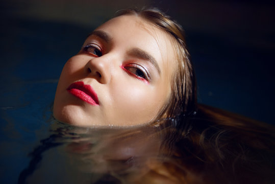 Glamorous brunette girl with colored make-up on closed eyes and clean skin in the pool close-up.