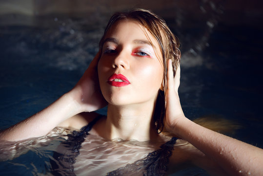 Glamorous brunette girl with color make-up and clean skin in the pool close-up.