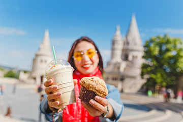 Young asian woman tourist drinking frappe sweet cold coffee and tasty muffin at the Budapest city...