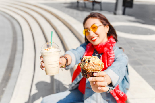 A female student on the street eating a snack of frappuchino and mafin, a concept of a modern lunch break