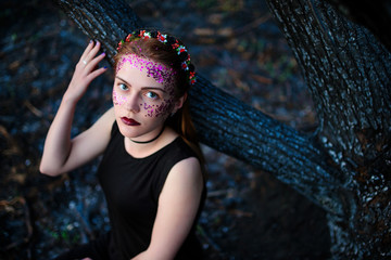 A young beautiful woman with a violet shine on her face stands near a burnt tree
