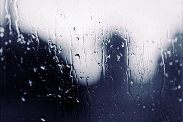 Water rain drops on the window glass on sunset. Shallow depth of field. Cityscape silhouette.