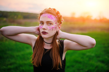 A young beautiful woman with a violet shine on her face standing on the grass and looking at the camera