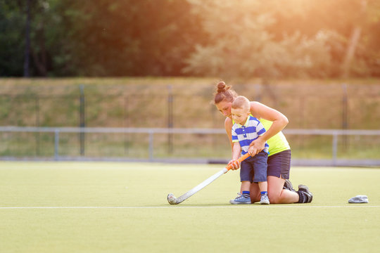 Small boy training playing field hockey with stick on the field with his mother