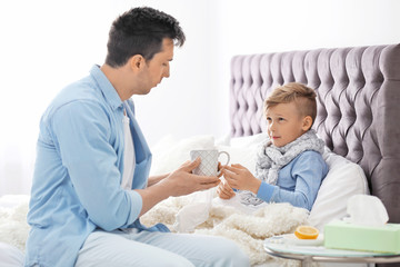 Father taking care of little son suffering from cold in bed