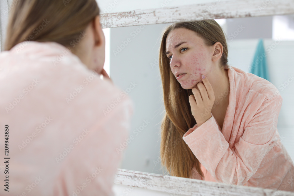 Wall mural young woman with acne problem near mirror in bathroom