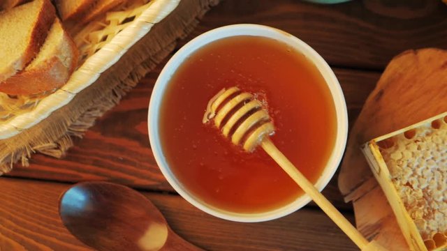 Honey pot and dipper at rustic table with bread, raisins, chamomile flowers and Honey comb, top view