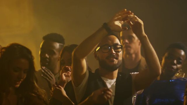 Medium shot of ecstatic multi ethnic crowd dancing and clapping hands during party in nightclub