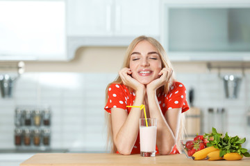 Young woman with glass of delicious milk shake in kitchen
