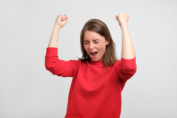 happy caucasian woman in red sweater exults pumping fists celebrates success or victory