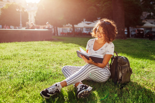 Beautiful college girl reading a book in campus park. Happy woman student learning outdoors