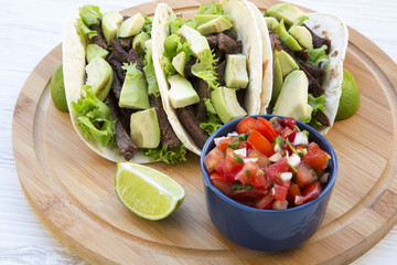 Tacos with salsa on the bamboo board over white wooden background, side view. Mexican food. Close-up.