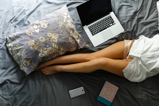 Slim, perfect and beautiful crossed woman legs on bed. Cropped image of erotically lying on bed beautiful woman in bedroom. Women using laptop and wearing her sexy relaxed at her bed. Top view