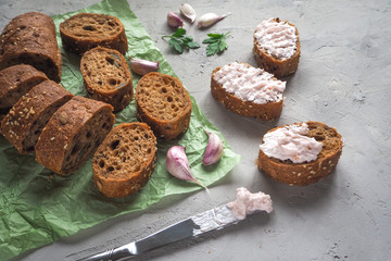 Snack with garlic cream on sliced whole wheat baguette on grey cement background.