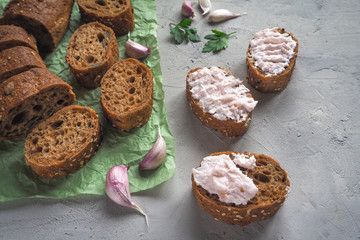 Snack with garlic cream on sliced whole wheat baguette on grey cement background.