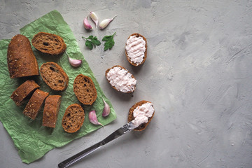 Snack with garlic cream on sliced whole wheat baguette on grey cement background.