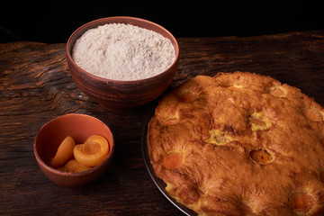A bowl with flour and apricot cake on a wooden background