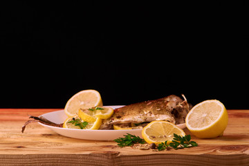 Baked fish with lemon, spices and herbs on white plate on wooden background without head