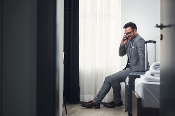 Happy businessman talking over smart phone at hotel room 