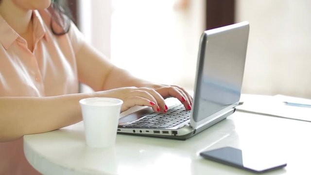A woman is sitting in a cafe drinking coffee and working on a laptop. slow mo. The camera moves to dolly from the right to the left.