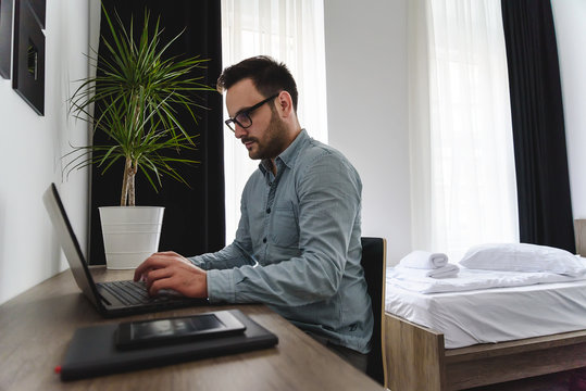 Businessman using laptop computer, working at his hotel room. Traveling for work. 