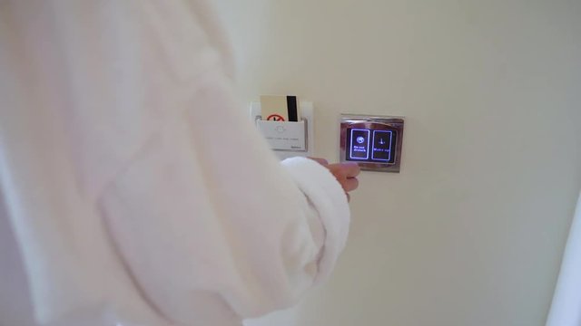 woman in a white coat inserting electronic key card in power switch holder on wall in the hotel. Then push the button does not disturb on the smart touch screen.