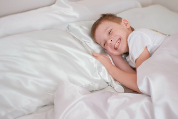 Obraz na płótnie Canvas Seven-year-old boy just woke up and laughs while lying in bed.