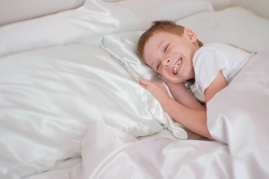 Seven-year-old boy just woke up and laughs while lying in bed.
