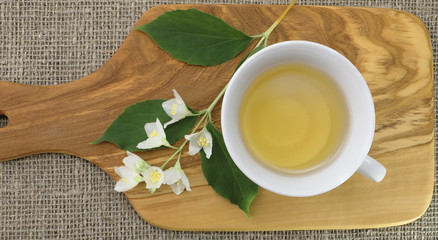 White glass cup of green tea with jasmine flowers on olive wooden background. Top view.