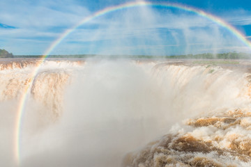 Wide angle landscape view of Iguazu waterfalls on a sunny day in summer with a rainbow. Photo taken from the Argentinian side at the Devil’s throat.