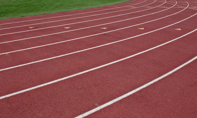 White painted running lanes on a red track with green grass